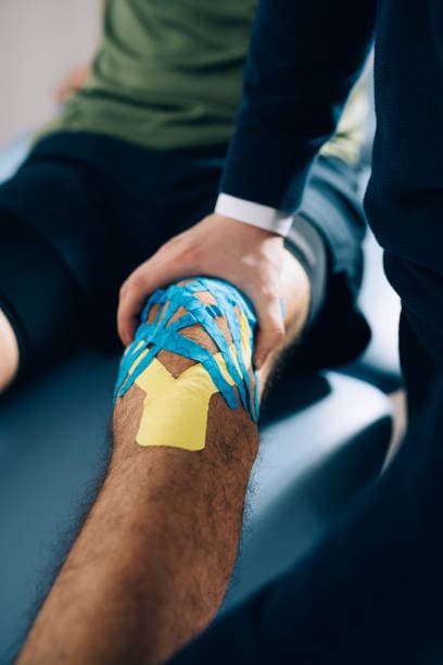 Fisioterapeuta aplicando vendaje neuromuscular en la rodilla de un paciente para fisioterapia de urgencia en un entorno clínico