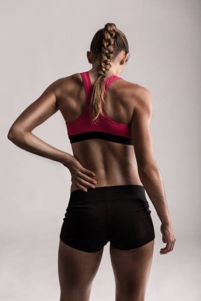 Atleta femenina con trenza y ropa deportiva lleva la mano a su espalda, lista para una sesión de fisioterapia deportiva.